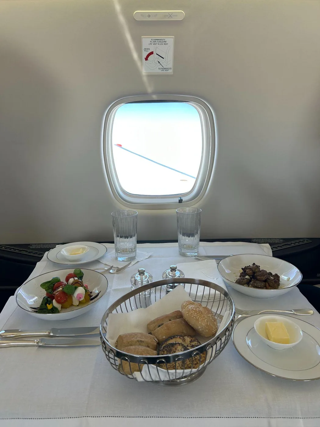 Gedeckter Tisch an Bord mit Salat, Brotkorb, Butter und Gläsern vor dem Kabinenfenster