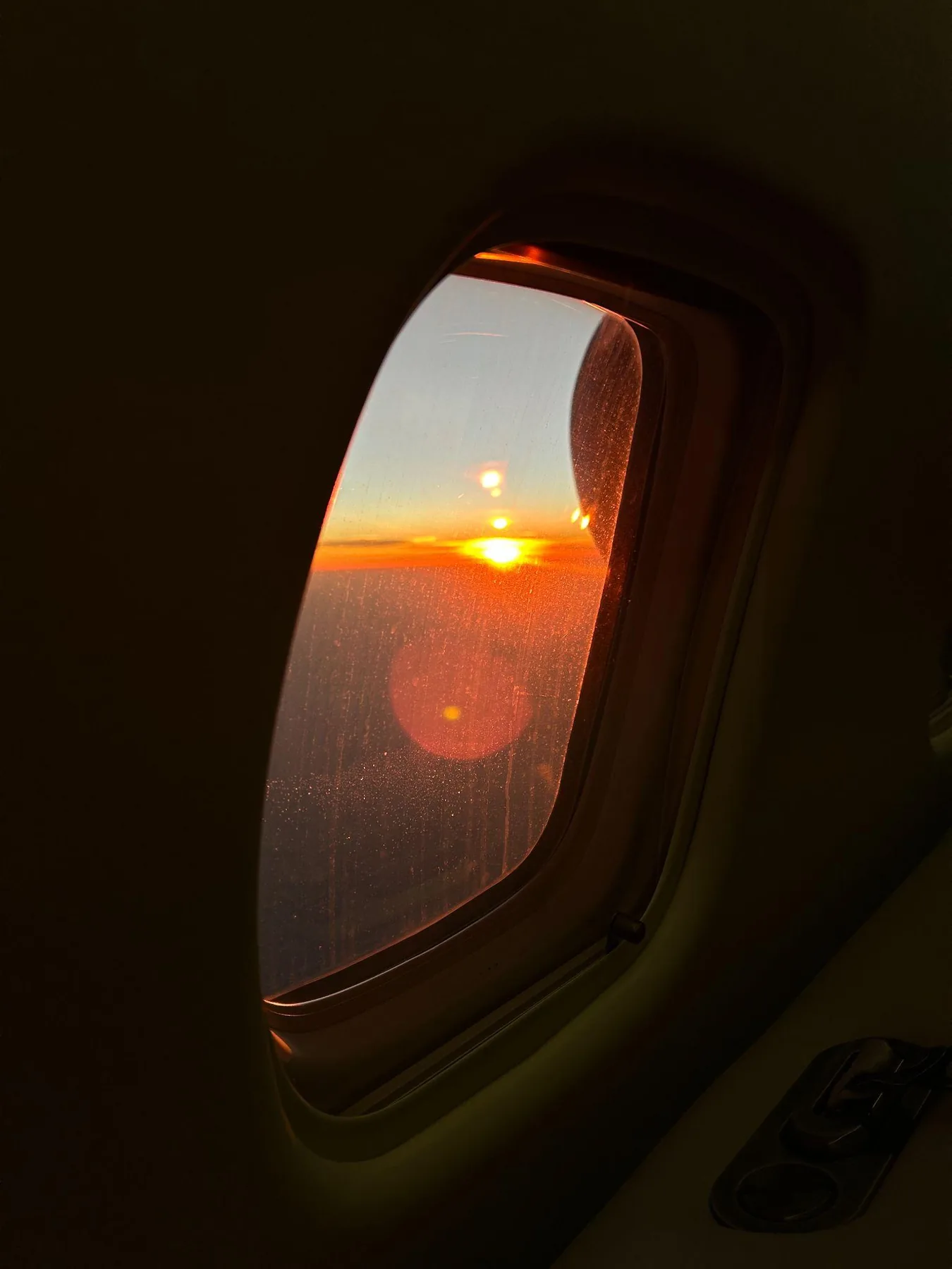 Sonnenuntergang über einer Wolkendecke, gesehen durch das Fenster des Privatjets