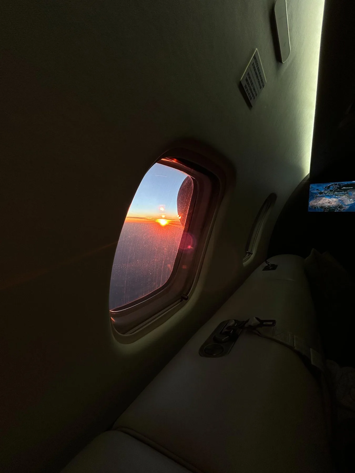 Abgedunkelte Kabine im Gegenlicht des Sonnenuntergangs, daneben der Bildschirm mit der Flugkarte