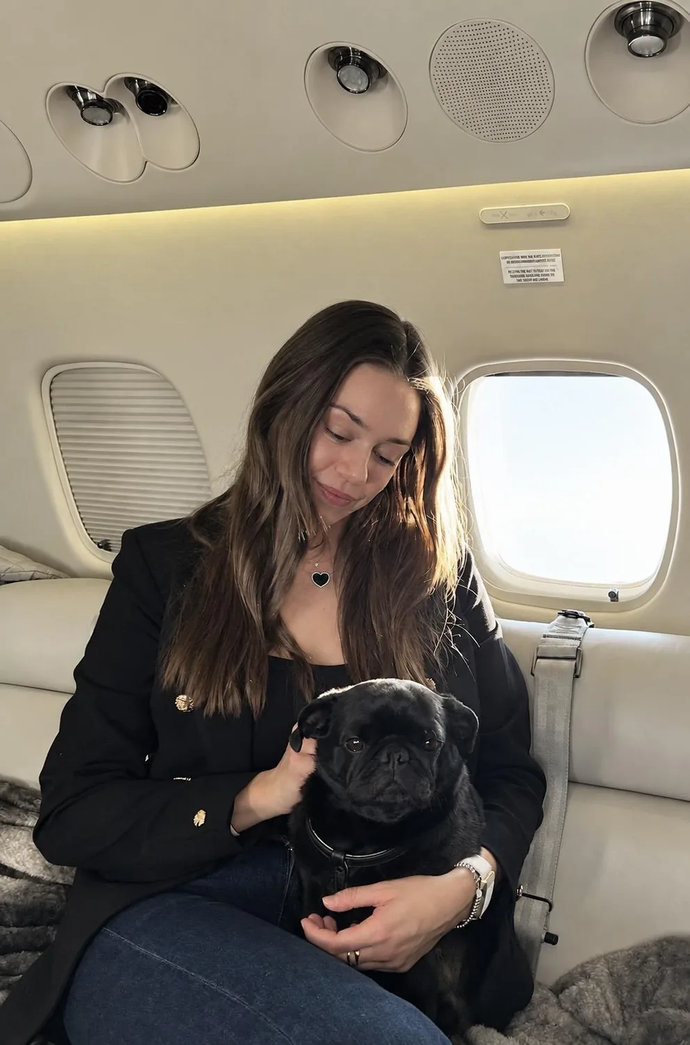 Die Gästin sitzt im Privatjet und hält ihren schwarzen Mops auf dem Schoß